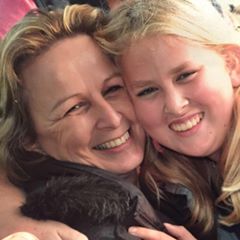 Two people with light hair, one adult and one child, are smiling and hugging each other closely, showing happiness and affection—perhaps celebrating a milestone like a keto weight loss journey together.